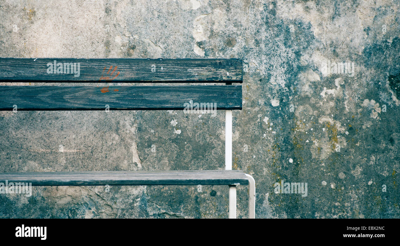 Leere Holzbank mit roten Handabdruck vor verwitterte Steinmauer. Stockfoto