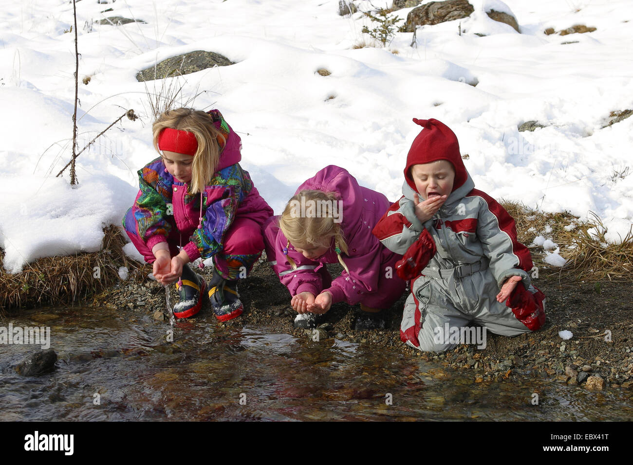 Kinder im Winter trinken klares Wasser aus einer kalten Gebirgsbach Stockfoto