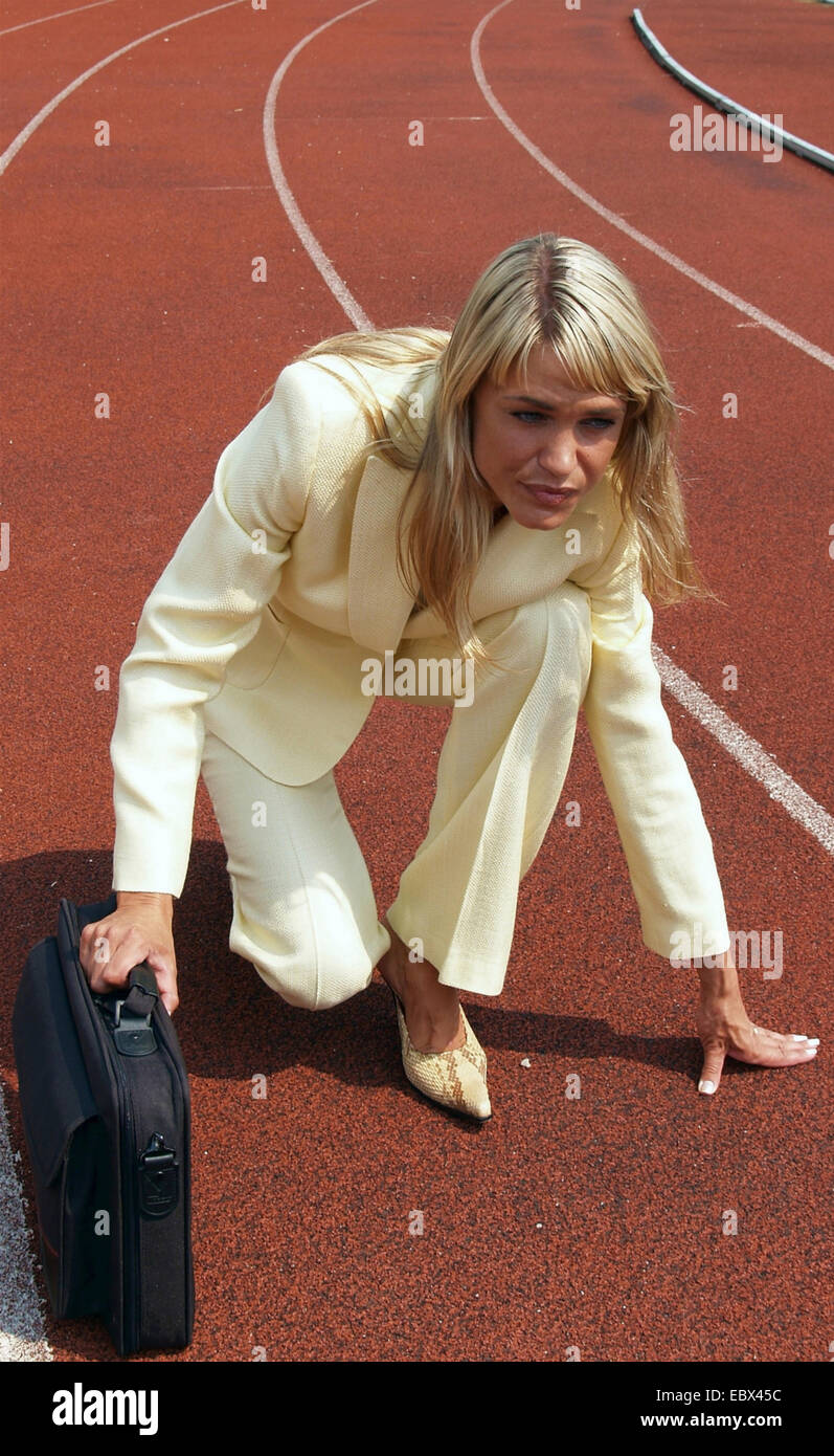 Business-Frau in einem Hosenanzug mit einer Brirfcase in die Startposition auf einer Tartanbahn im Sportstadion Stockfoto