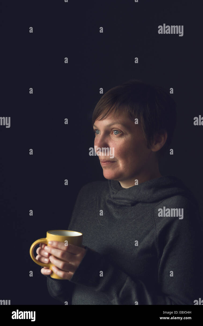 Schöne kaukasischen erwachsenen Frau trinken Kaffee im dunklen Raum. Selektiven Fokus mit geringen Schärfentiefe. Stockfoto