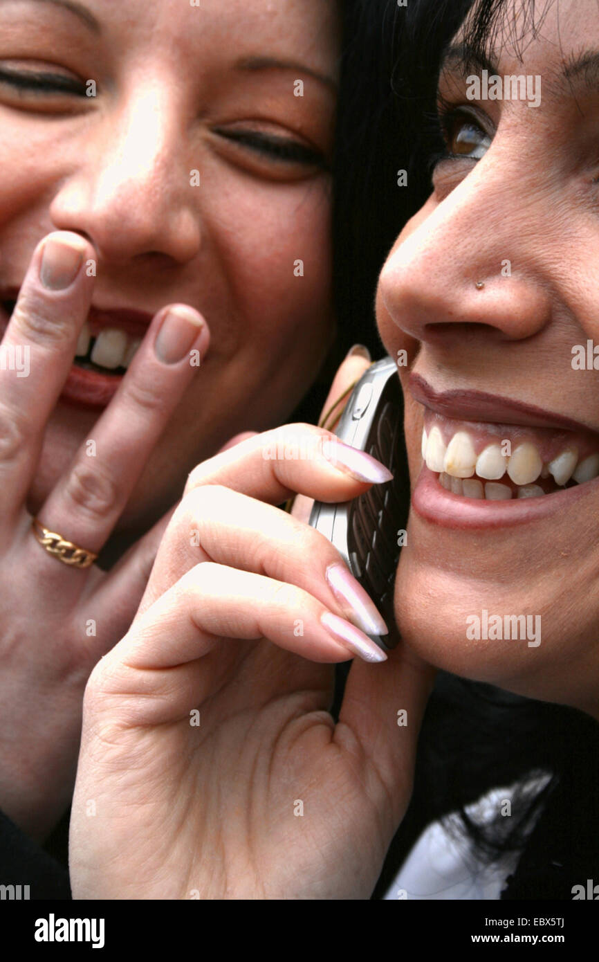 zwei lächelnde junge Frauen, eine reden über Handy Stockfoto