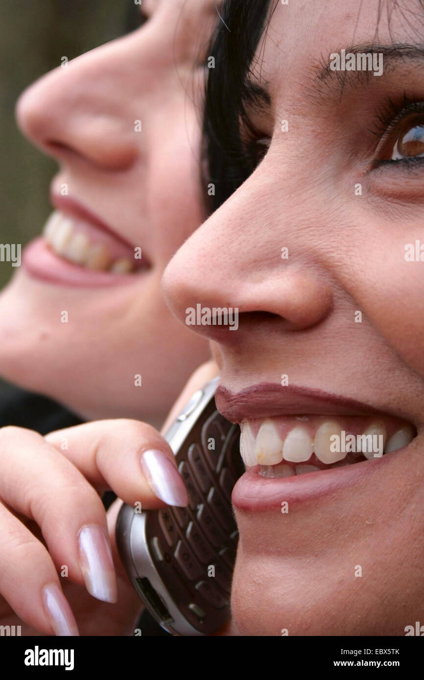 zwei lächelnde junge Frauen, eine reden über Handy Stockfoto