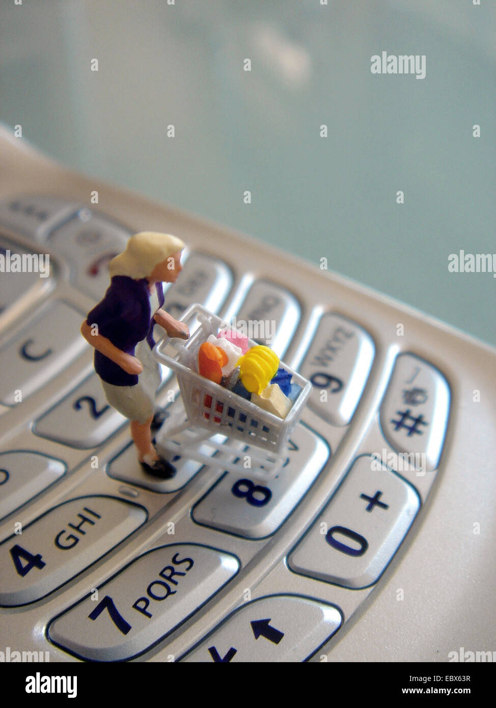 symbolisches Bild für Kauf von Handy, kleine Figur auf einem Celllular mit caddy Stockfoto