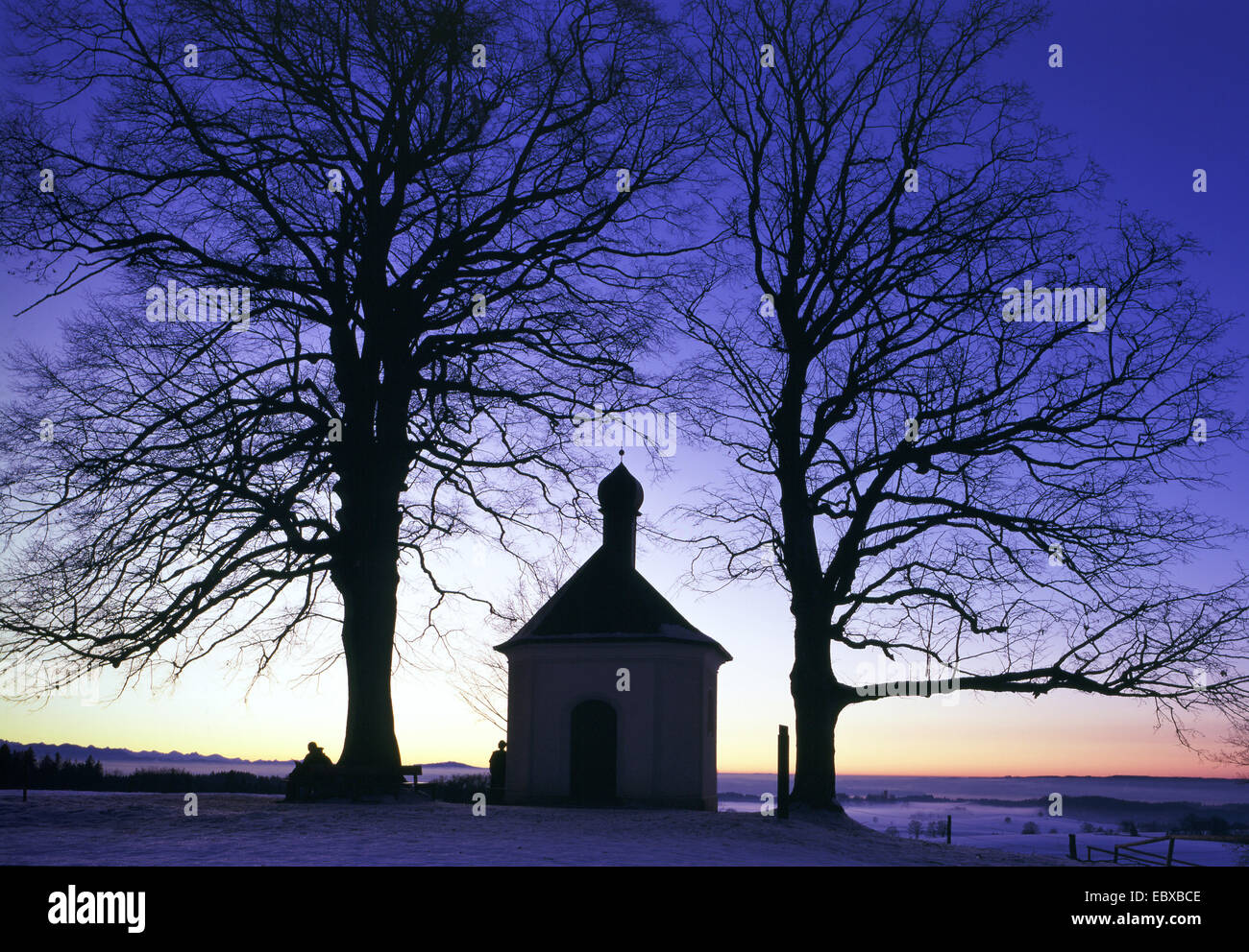 kleine Kapelle bei Sonnenuntergang, im Winter zwischen zwei Bäumen, Deutschland Stockfoto