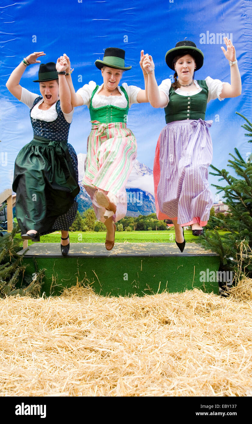 drei glückliche steirische Frauen springen hand in auf einem Volksfest in traditionellen Kostümen Stockfoto