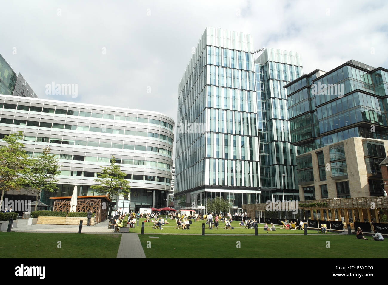 Sonniger Blick in den Himmel, um "3 Hardman Street" Leute sitzen Liegestühle weiß grün Grass Hardman Quadrat, Spinningfields, Manchester Stockfoto