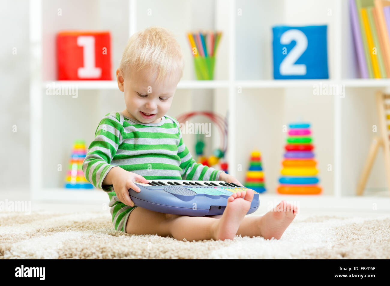 Glückliches Kind Kleinkind Jungen Spaß spielen Klavier Spielzeug sitzen am Boden im Kinderzimmer Stockfoto