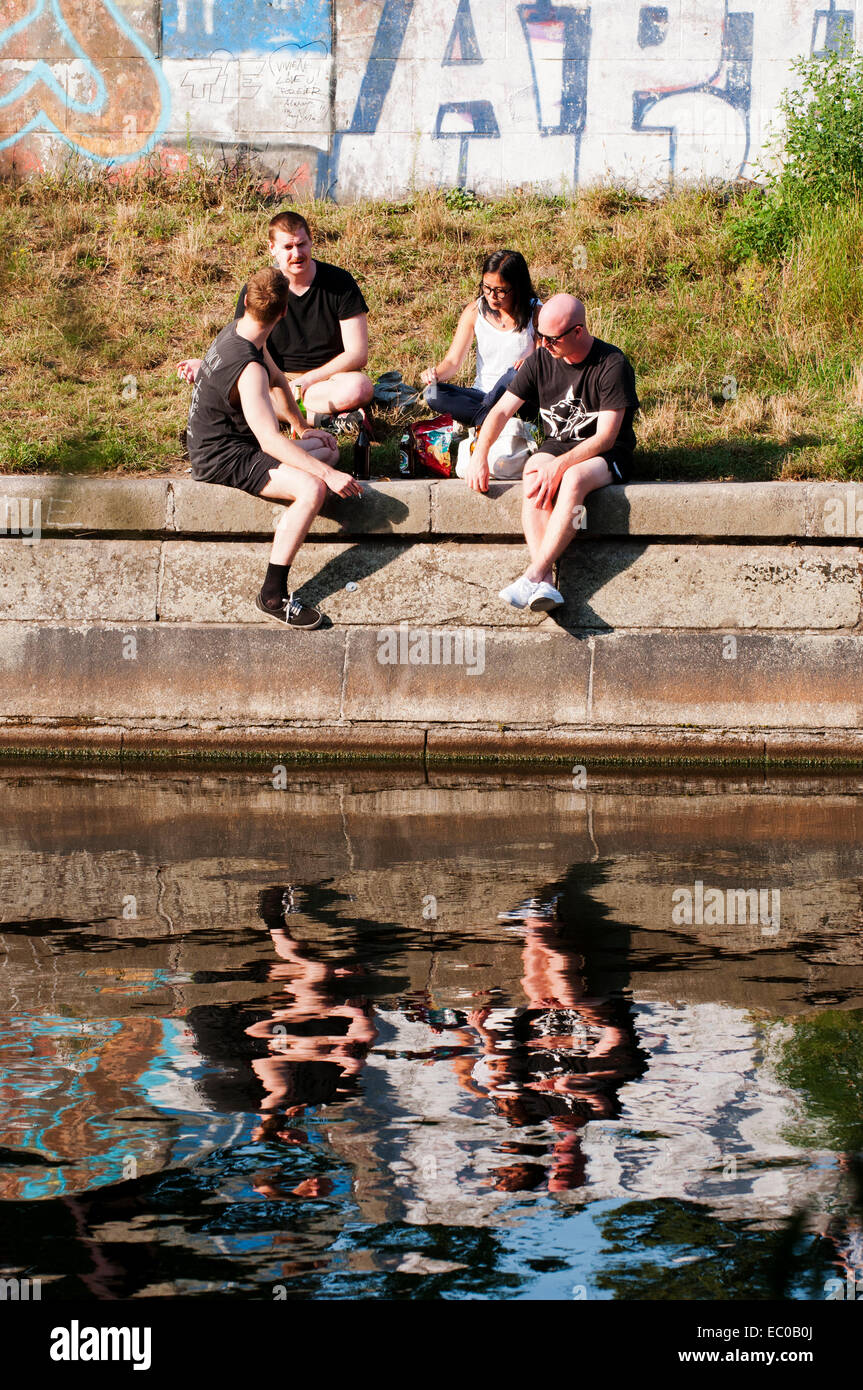 Junge Leute sitzen neben Landwehrkanal, angrenzend an Kreuzberg und Hermannplatz. Stockfoto