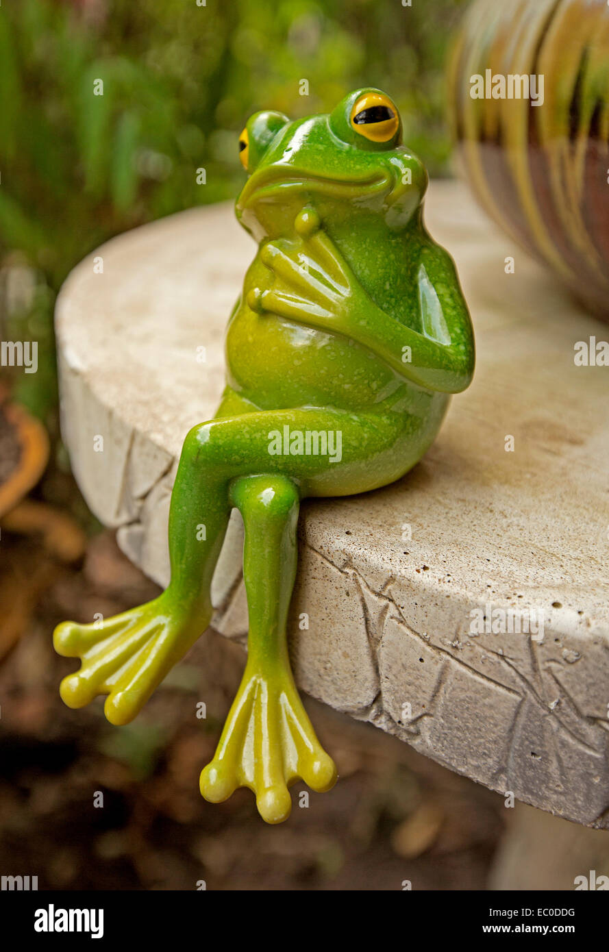 Komischen grünen Frosch Ornament sitzen mit gekreuzten Beinen auf der Tischkante mit Ausdruck & Pose als obwohl tief in Gedanken. Stockfoto