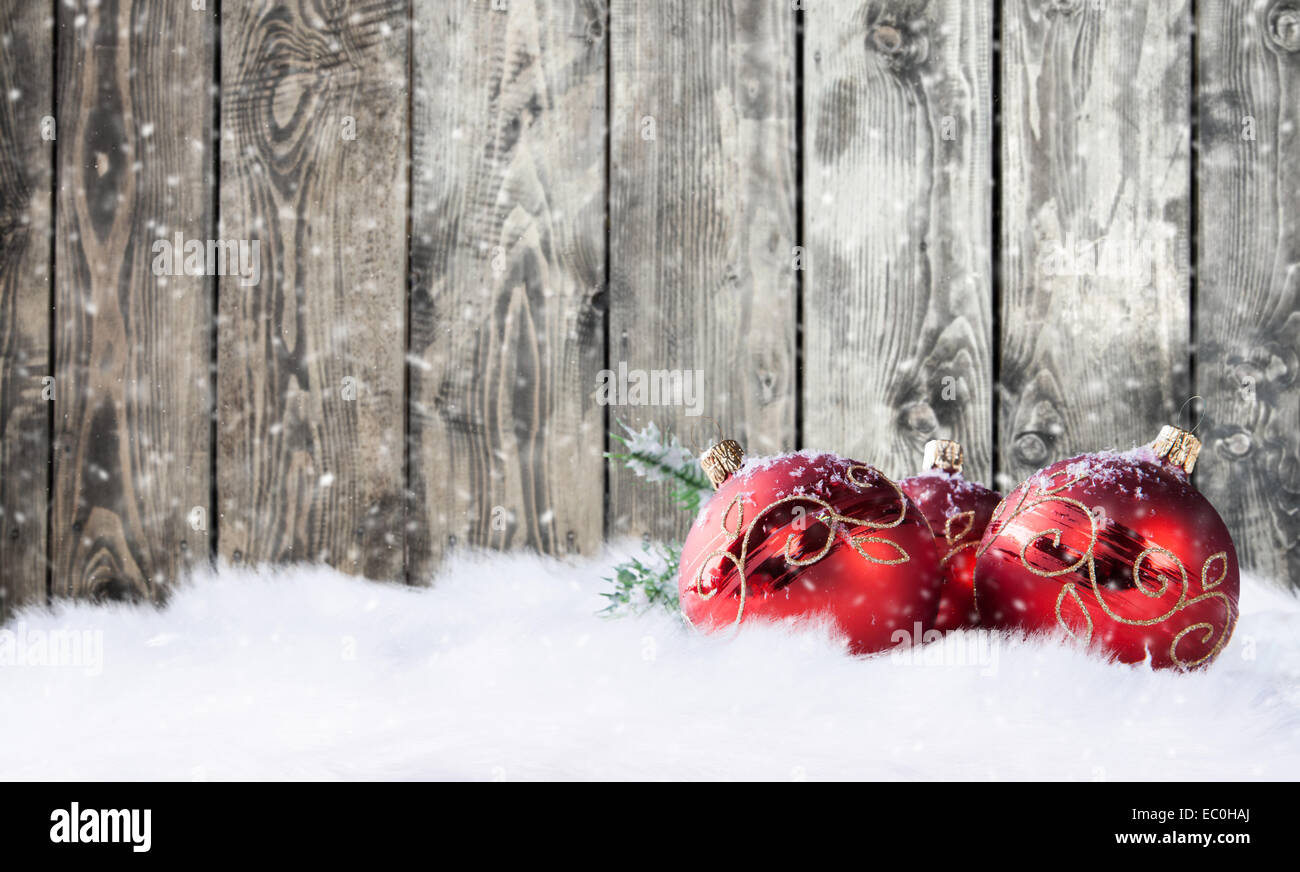 Dekorative rote Weihnachtskugeln auf Schnee mit Holzbohlen als Hintergrund Stockfoto