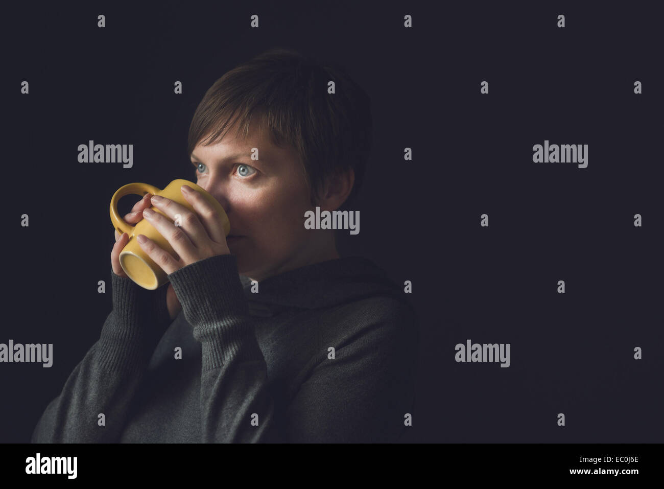 Schöne kaukasischen erwachsenen Frau trinken Kaffee im dunklen Raum.  Selektiven Fokus mit geringen Schärfentiefe. Stockfoto