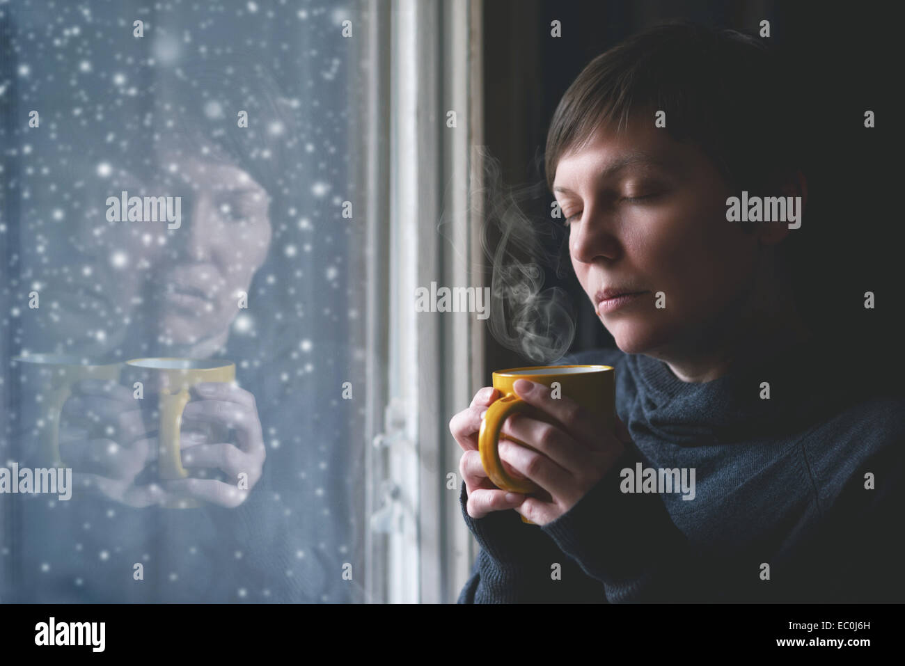 Einsame Frau trinkt Kaffee am Fenster ihres Wohnzimmers während der Schnee fällt außerhalb. Selektiven Fokus mit Stockfoto