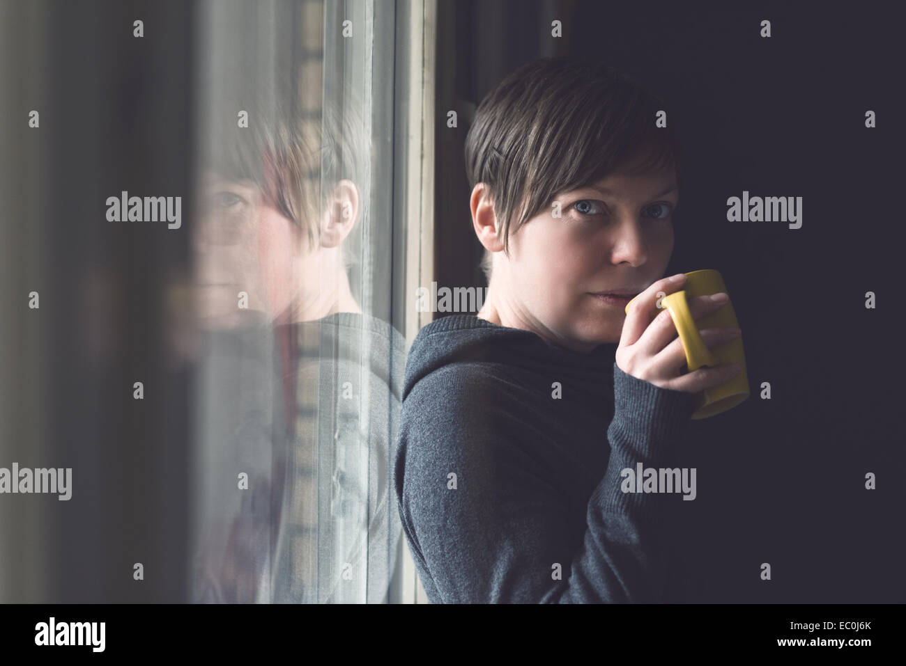 Schöne kaukasischen erwachsenen Frau trinken Kaffee im dunklen Raum durch das große Fenster. Selektiven Fokus mit geringer Tiefe f Stockfoto