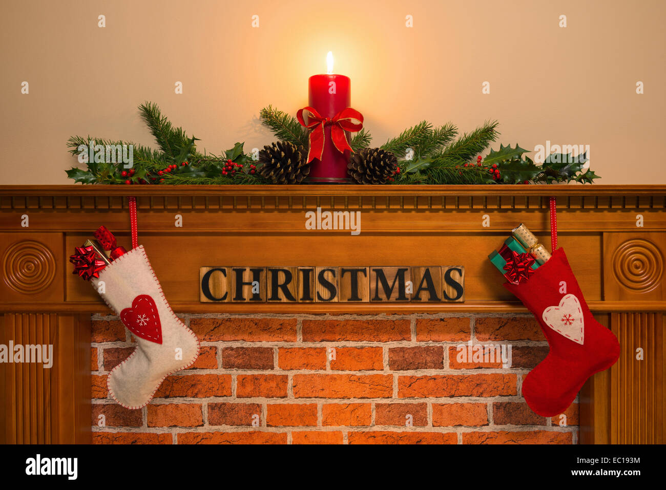 Kaminsims mit rote Kerze und frischen Kranz hergestellt aus Stechpalme, zwei Strümpfe voller Geschenke hängen über dem Kamin mit dem w Stockfoto