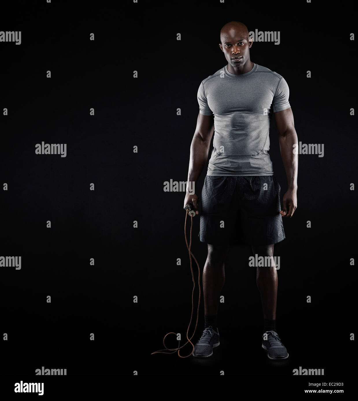 Studio shot der Fit und muskulöser Mann mit springen Seil stehend auf schwarzem Hintergrund. Afroamerikanische Männermodel mit Textfreiraum. Stockfoto