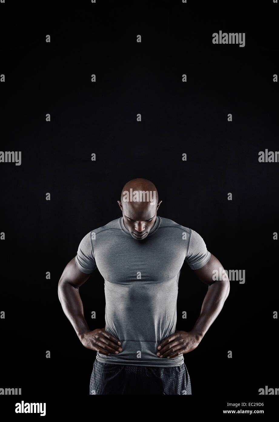 Porträt von muskulösen jungen Mann in Sportbekleidung stehend mit den Händen auf den Hüften nach unten auf schwarzem Hintergrund. Stockfoto
