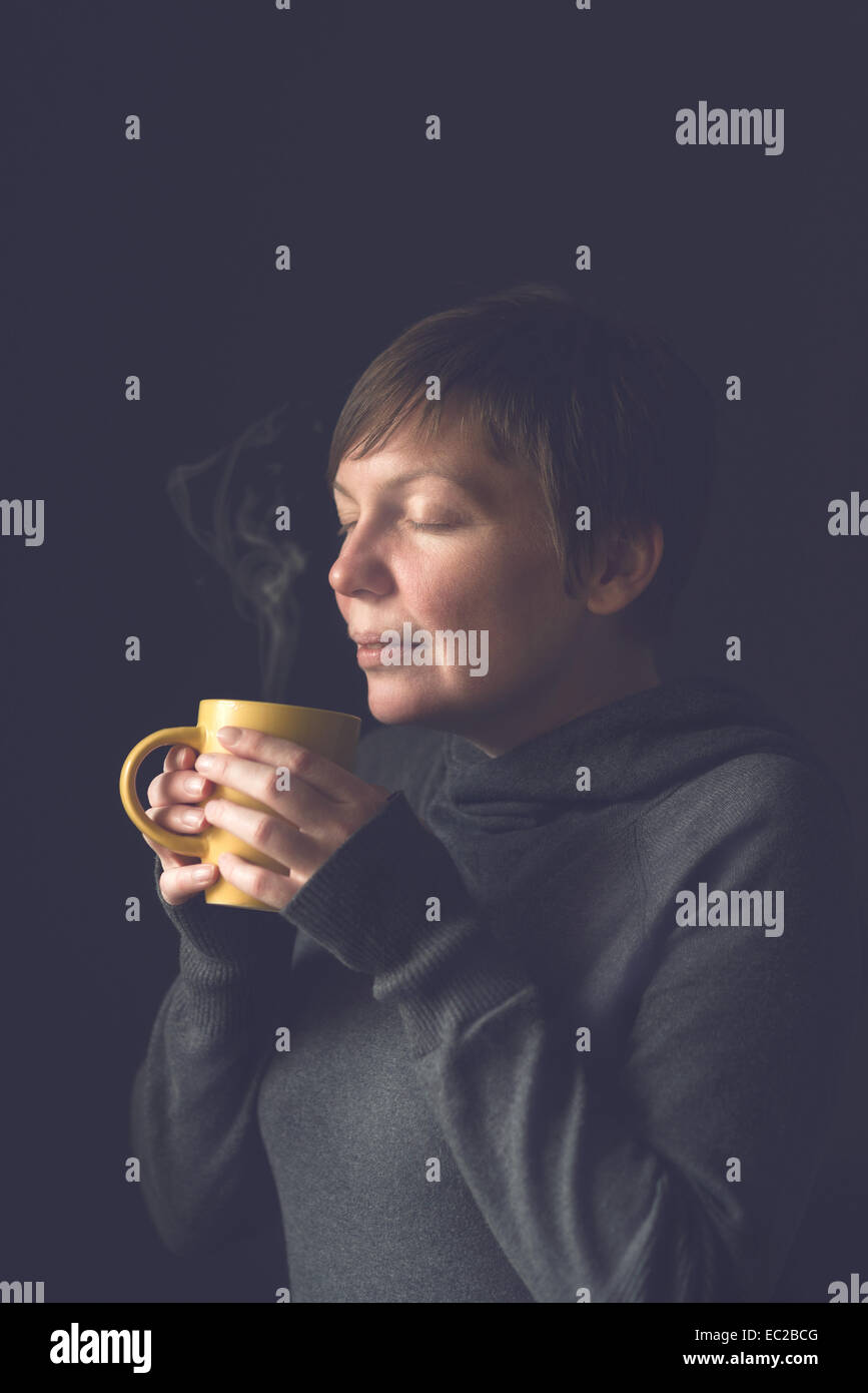 Kaukasische adult Woman with duftenden Tasse Kaffee im dunklen Raum. Selektiven Fokus mit geringen Schärfentiefe. Stockfoto