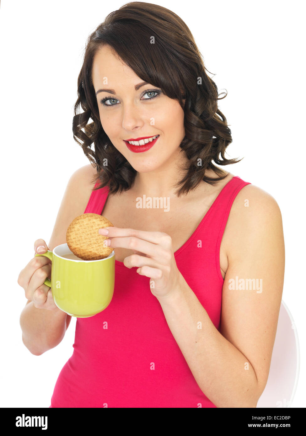 Sicher glückliche junge Frau Tauchen oder Dunking einen Keks in eine Tasse Tee oder Kaffee trinken entspannende Pause Isoliert gegen einen weißen Hintergrund Stockfoto
