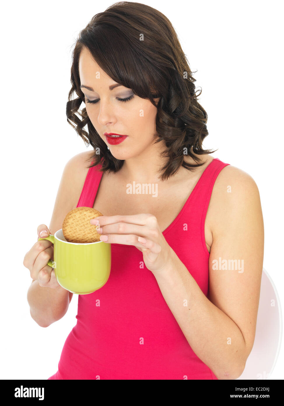 Sicher glückliche junge Frau Tauchen oder Dunking einen Keks in eine Tasse Tee oder Kaffee trinken entspannende Pause Isoliert gegen einen weißen Hintergrund Stockfoto