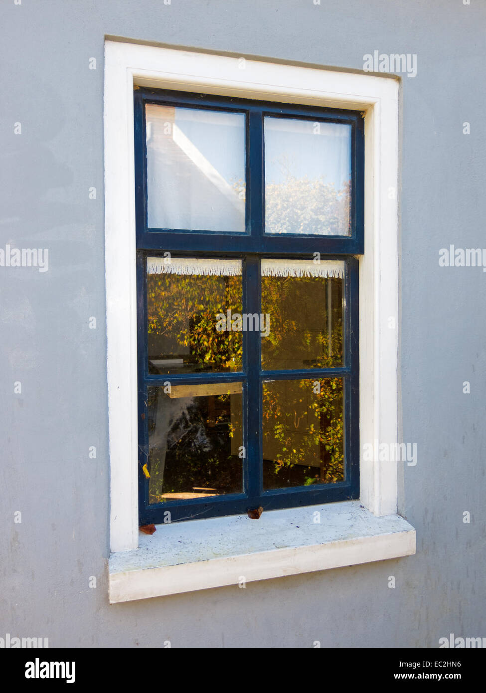 Einfaches Fenster in eine glatte verputzte Wand mit einer Reflexion der Herbst Blätter Stockfoto