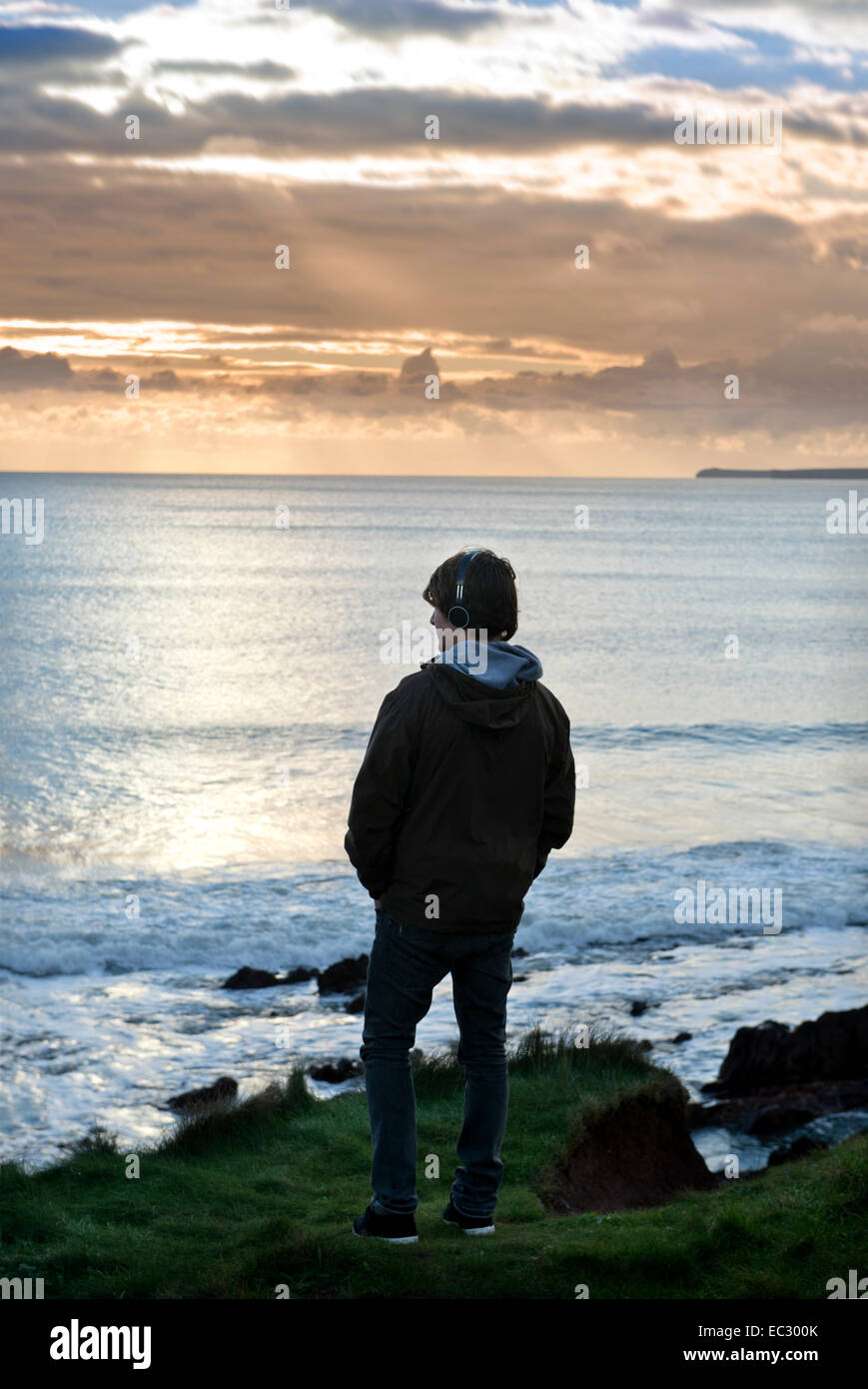Ein Teenager hört auf seinem iPod beim Betrachten der Aussicht bei Manorbier Bay in der Nähe von Tenby in Pembrokeshire, Wales UK Stockfoto