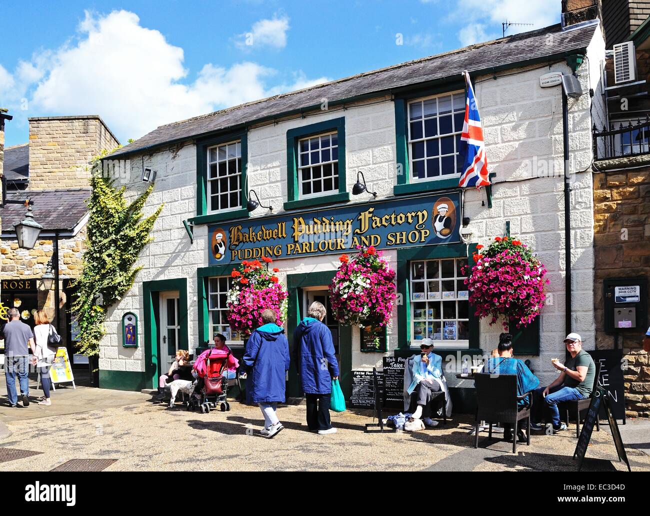 Touristen sitzen in einem Straßencafé außerhalb der Bakewell Pudding Fabrik im Zentrum Stadt, Bakewell, Derbyshire, England, Vereinigtes Königreich, Stockfoto