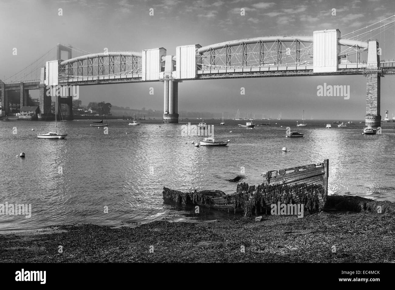 Ein verfallenes Holzboot liegt am Ufer des Flusses Tamar mit wunderschönen Royal Albert Bridge als Kulisse im Morgengrauen verstoßen, Stockfoto
