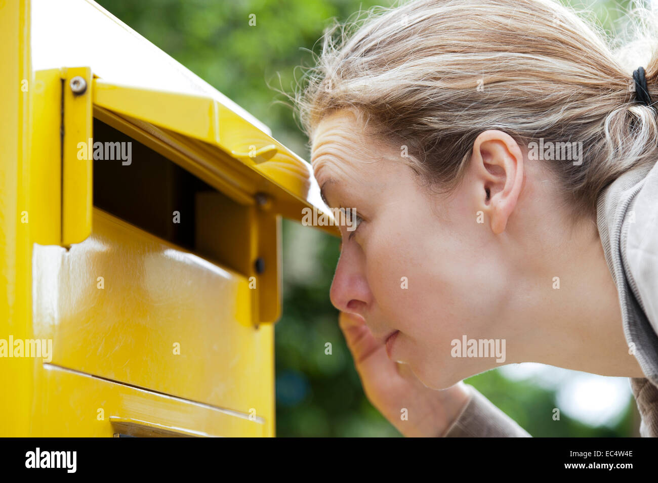junge Frau schaut neugierig in ein Postfach Stockfoto