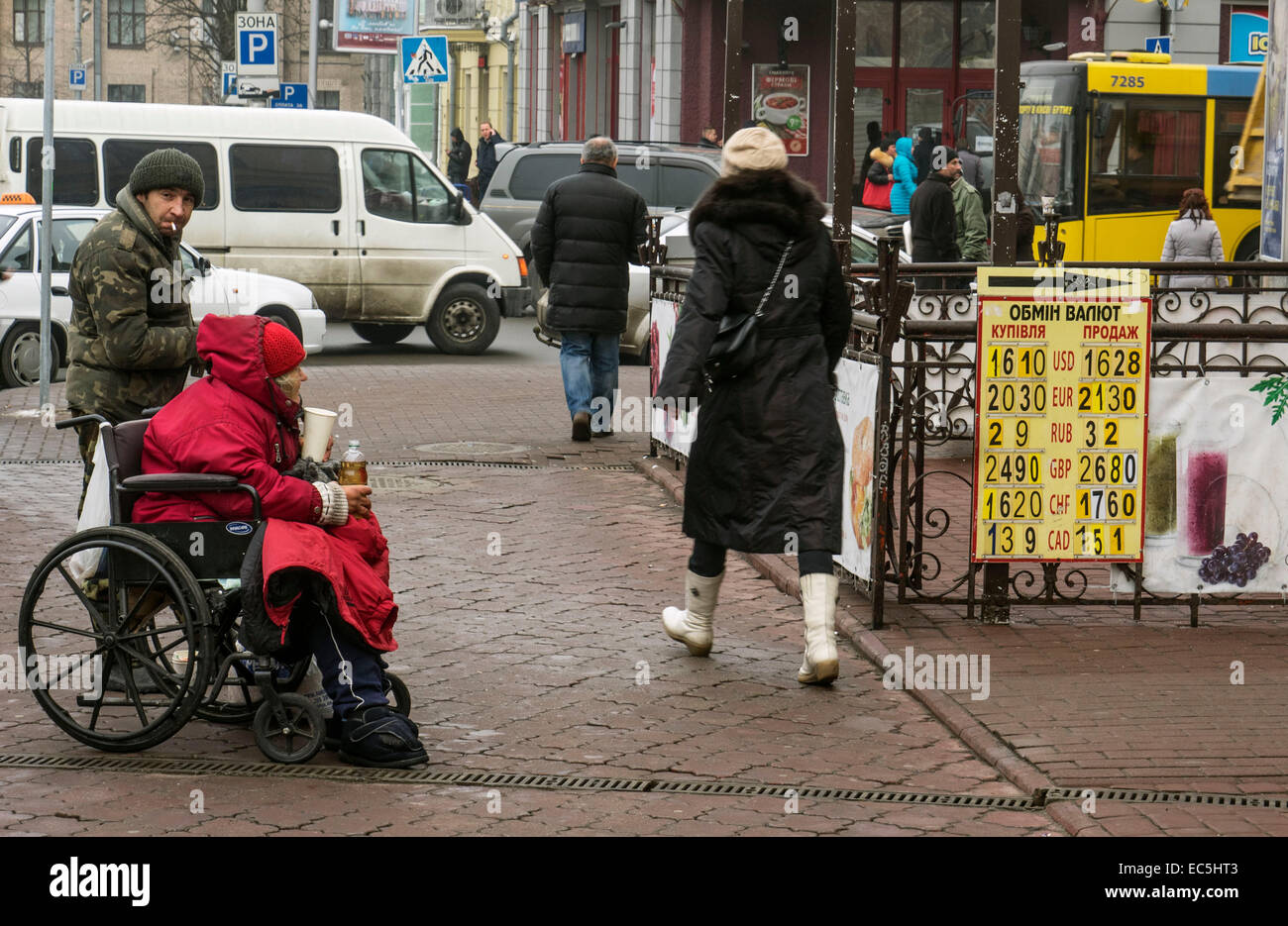 Bettler in einem Rollstuhl sitzt in der Nähe eine Wechselstube in der Nähe von Zeichen mit Wechselkursen - die Rate der nationalen Währung der Ukraine fiel wieder. Die Regierung hofft, ihn nach Erhalt der nächsten Tranche des IWF zu stabilisieren. Stockfoto