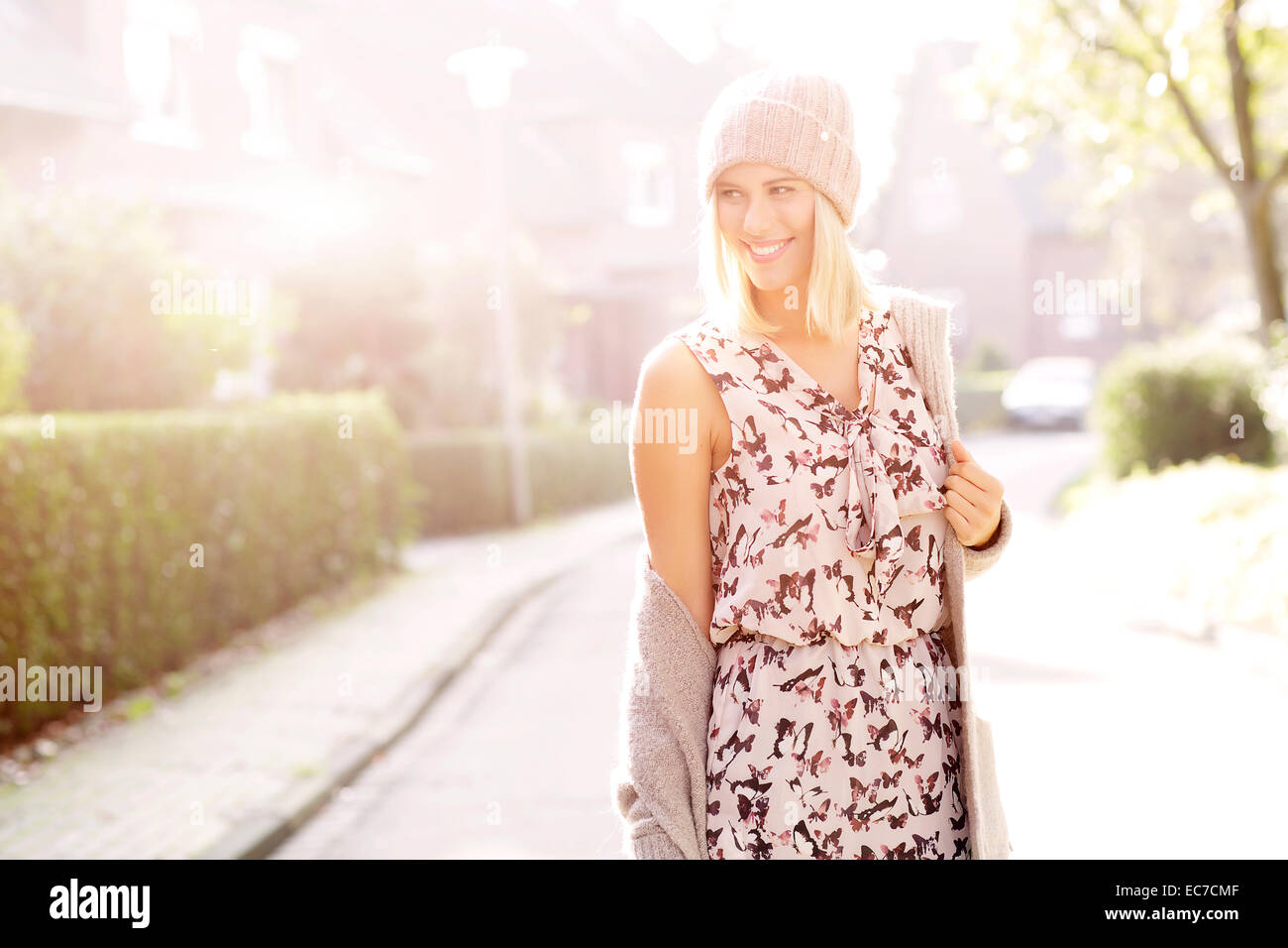 Porträt von lächelnden blonden Frau in gemusterten Kleid, Strickjacke und Wolle Kappe Stockfoto