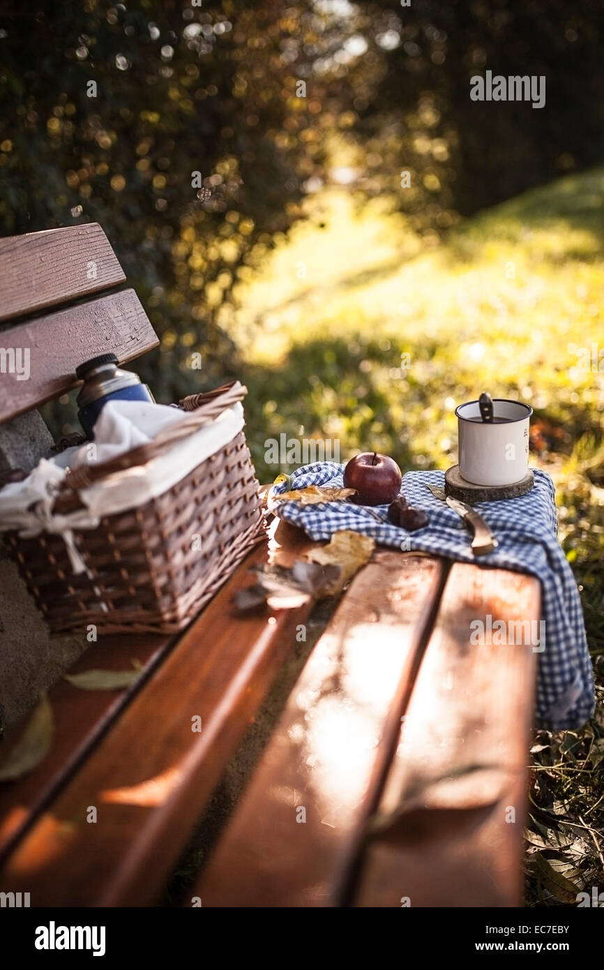 Kaffee, Apfel, Picknick-Korb und Herbstlaub auf Holzbank Stockfoto