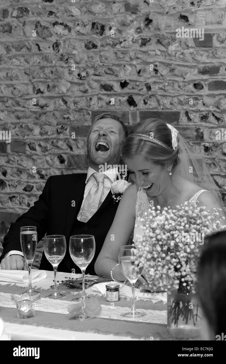 Braut und Bräutigam in Gelächter ausbrechen in die nach dem Abendessen Rede. Blumen und Champagner-Gläser auf dem Tisch. Stockfoto