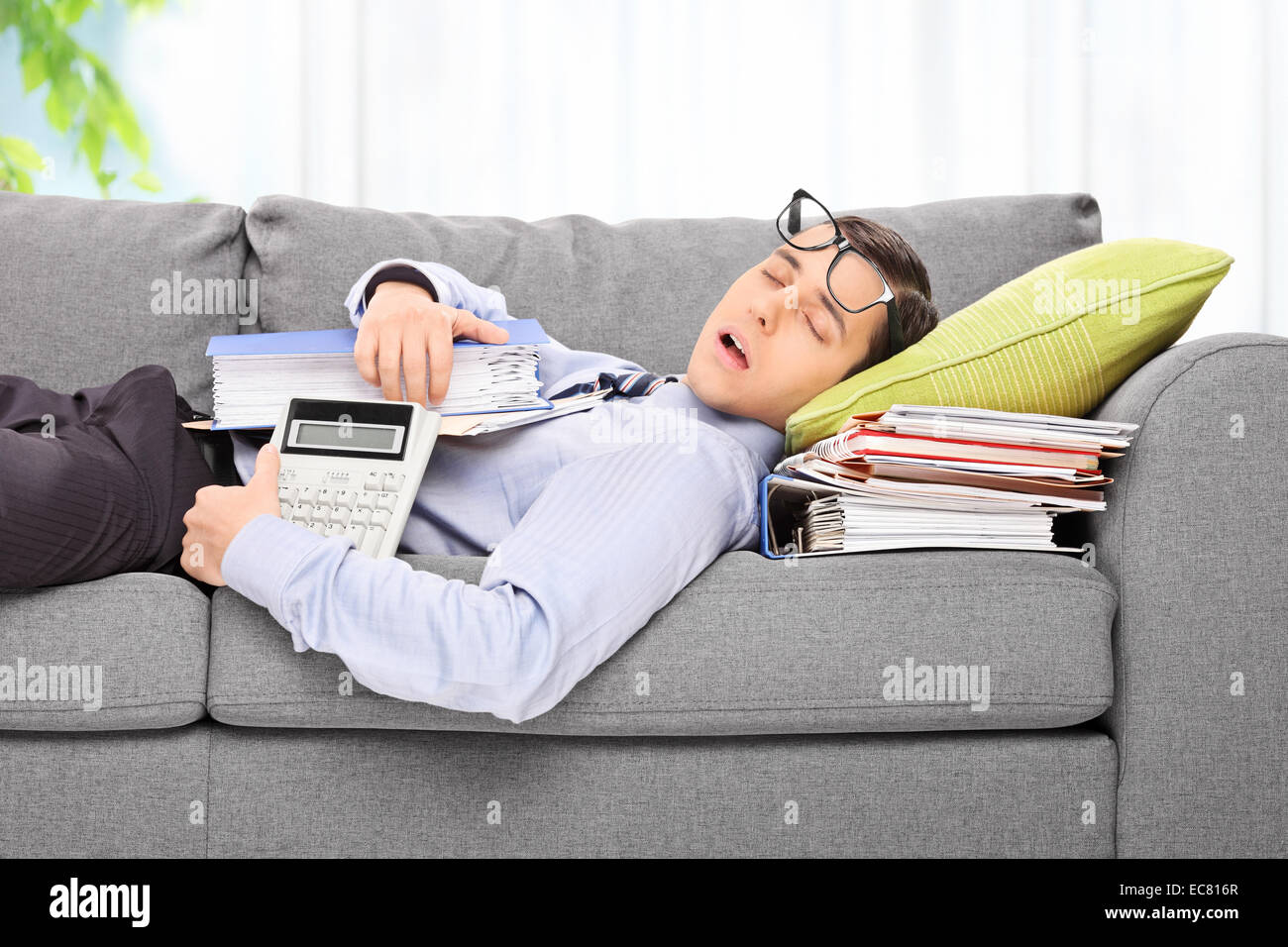 Müde Mitarbeiter schlafen auf einem Sofa im Büro auf einem Stapel von Dokumenten Stockfoto