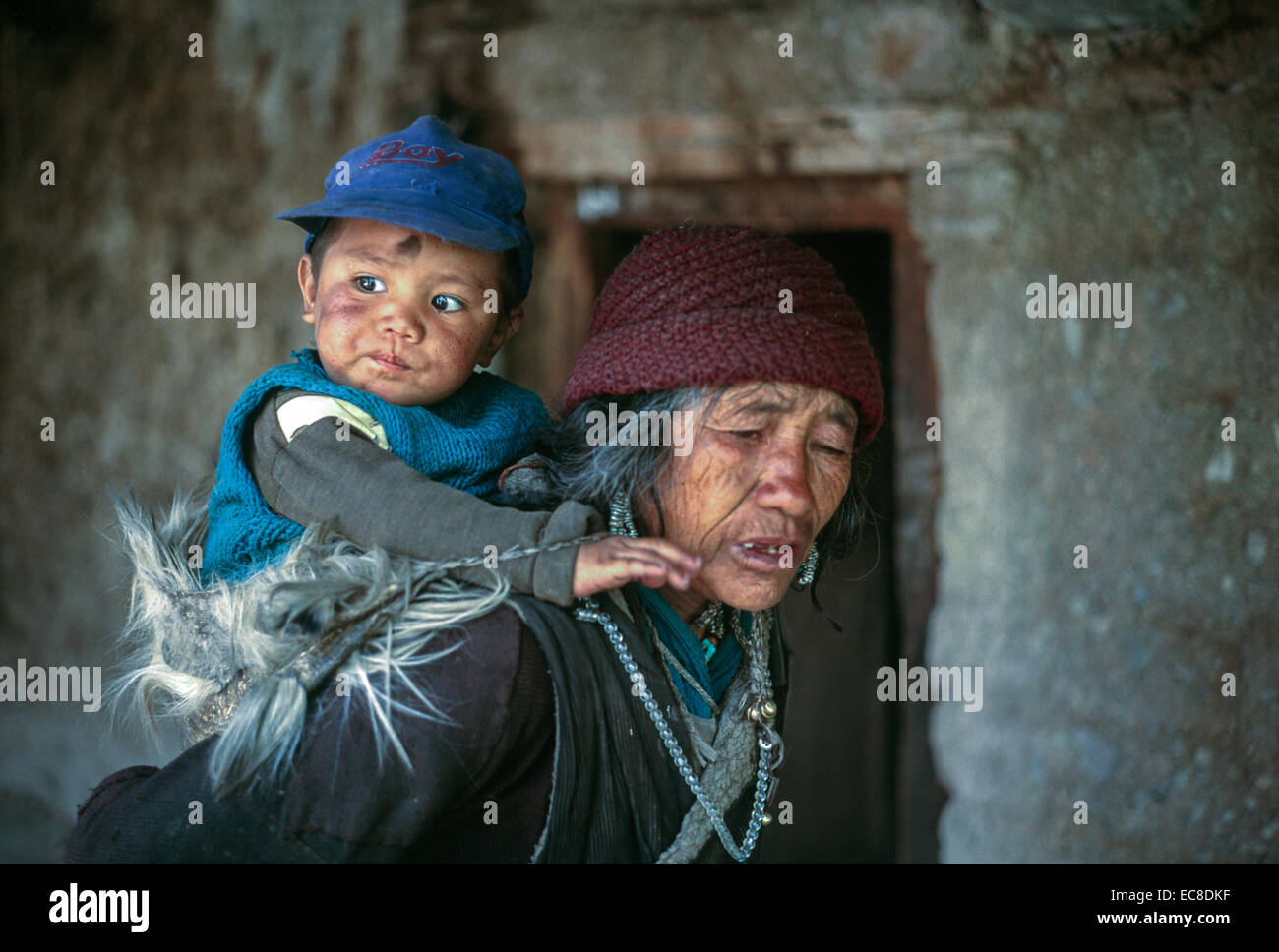 Ladakh-Tibet alte Frau, die junge Papoose Baby traditionelle Ziege Haut Gonca Robe Perlen traditionelles Haus Tür Stockfoto