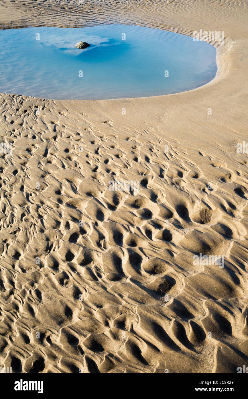 Fließen Sie Muster und Pool in einem sandigen Strand, links von der zurückweichenden Flut Stockfoto