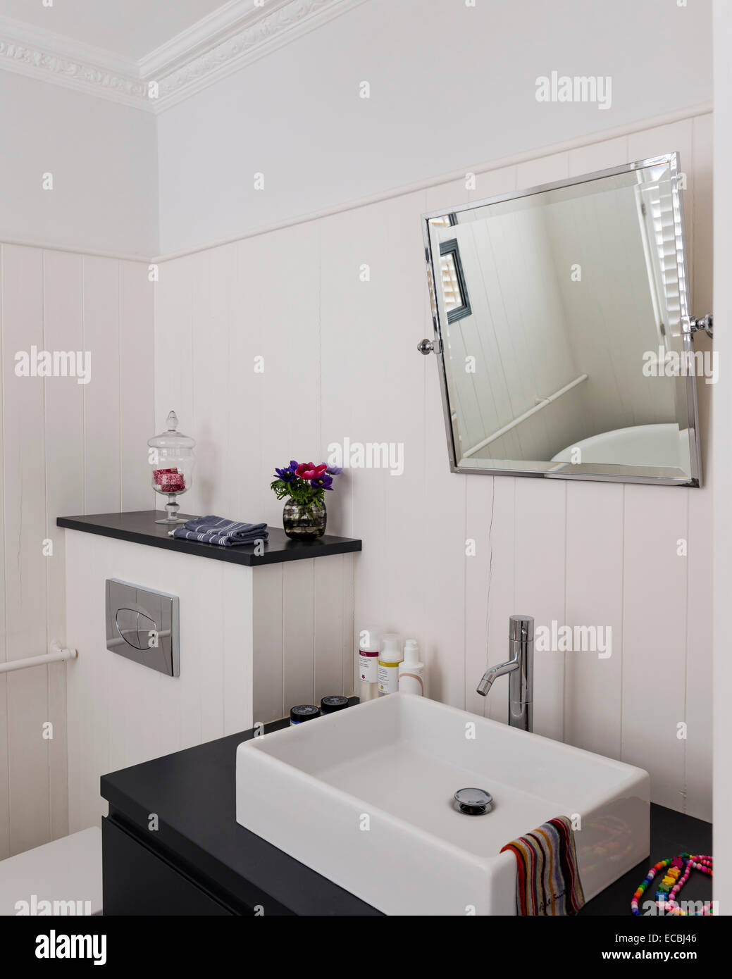 Moderne Waschbecken und abgewinkelten Spiegel im Badezimmer mit weißen Holzverkleidung Stockfoto