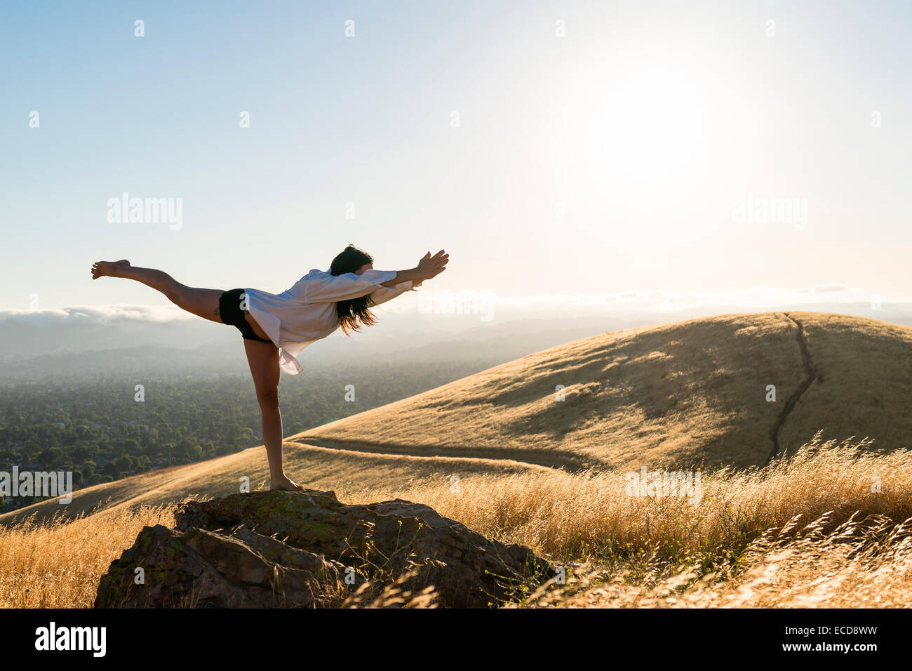 Frau in Yoga-Pose in einem Feld von golden Grass in Sonne verwöhnten Hügel von Kalifornien. Stockfoto