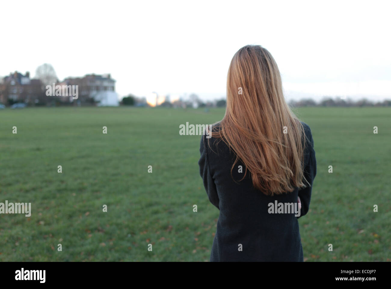 Hintere Ansicht Schuss eine junge Frau steht auf der Suche in die Ferne in einem Park. Stockfoto