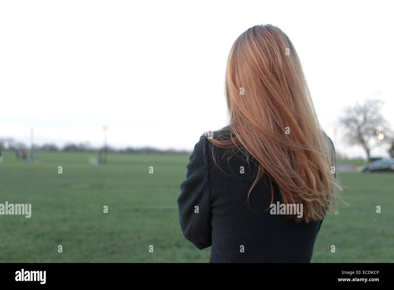 Hintere Ansicht Schuss eine junge Frau steht auf der Suche in die Ferne in einem Park. Stockfoto