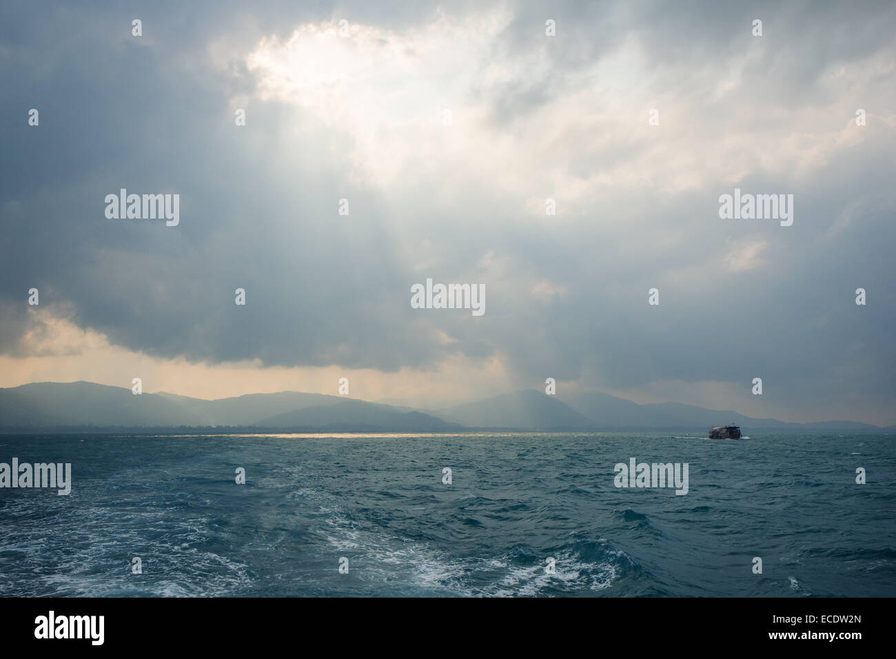 Sonnenstrahlen durch Loch in den Wolken über Meer und ein Schiff, Silhouette des hügeligen Koh Samui, Thailand Stockfoto