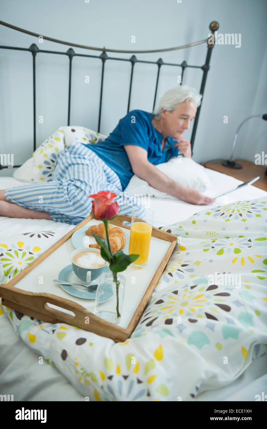 Reifer Mann mit Frühstück im Bett mit digital-Tablette, Lächeln Stockfoto