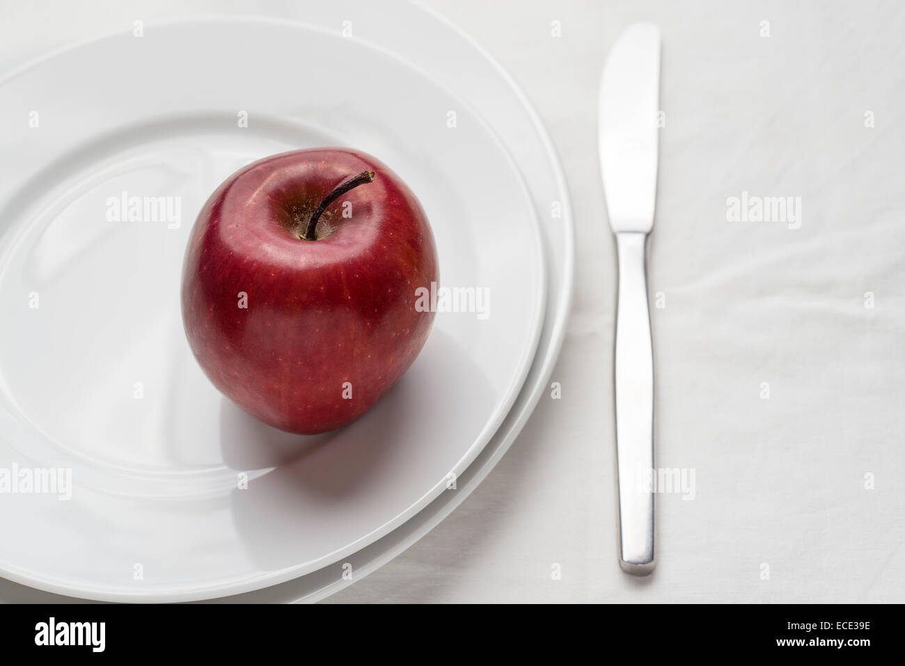 roter Apfel auf Platte und weiße Tischdecke Stockfoto