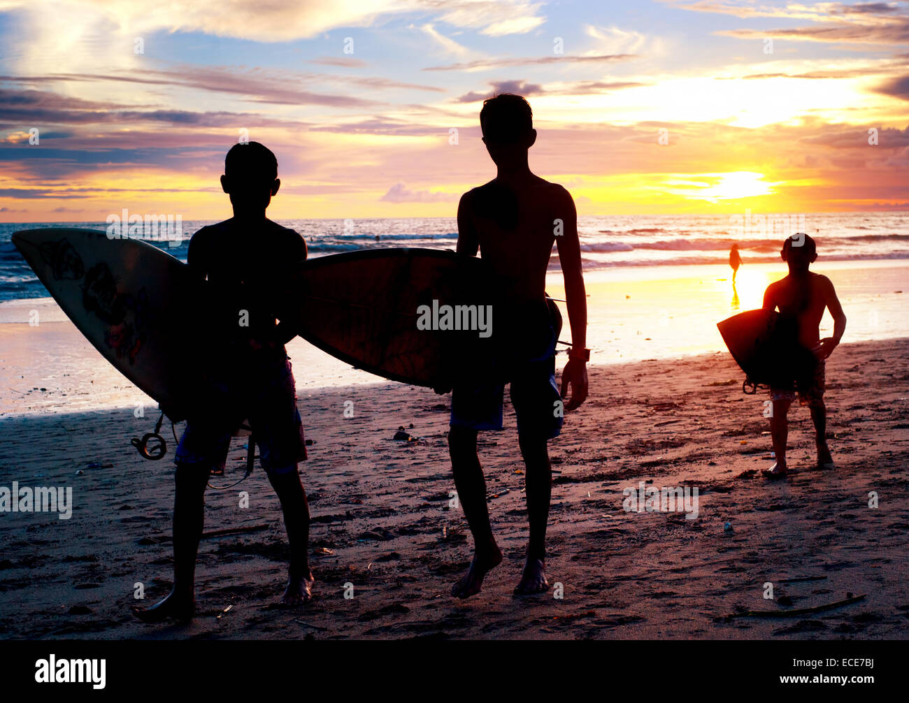 Lokalen Jungs mit einem Surfbretter bei Sonnenuntergang am Strand. Bali, Indonesien Stockfoto