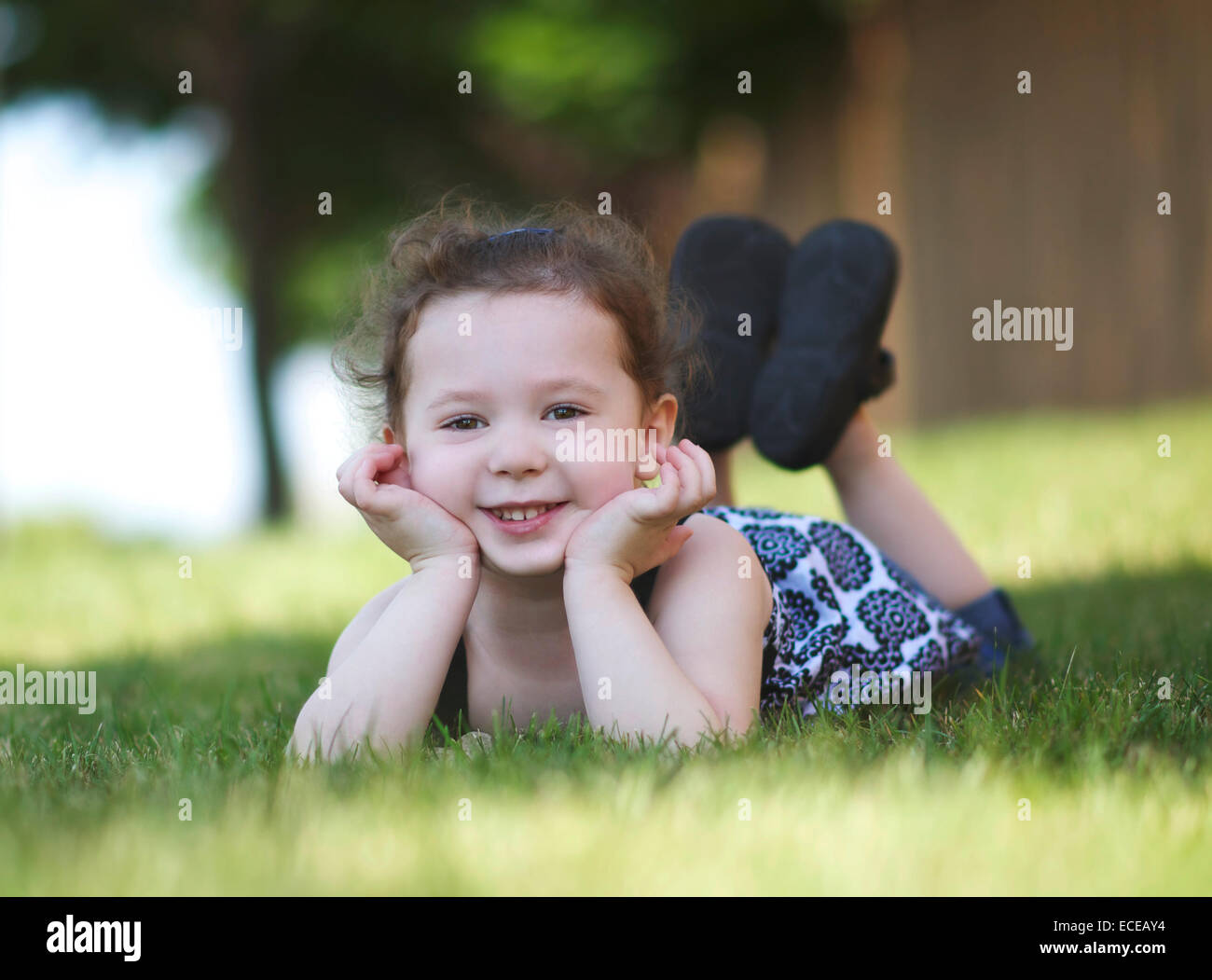 Lächelndes Mädchen, das auf Gras liegt und sich auf Ellbogen stützt Stockfoto