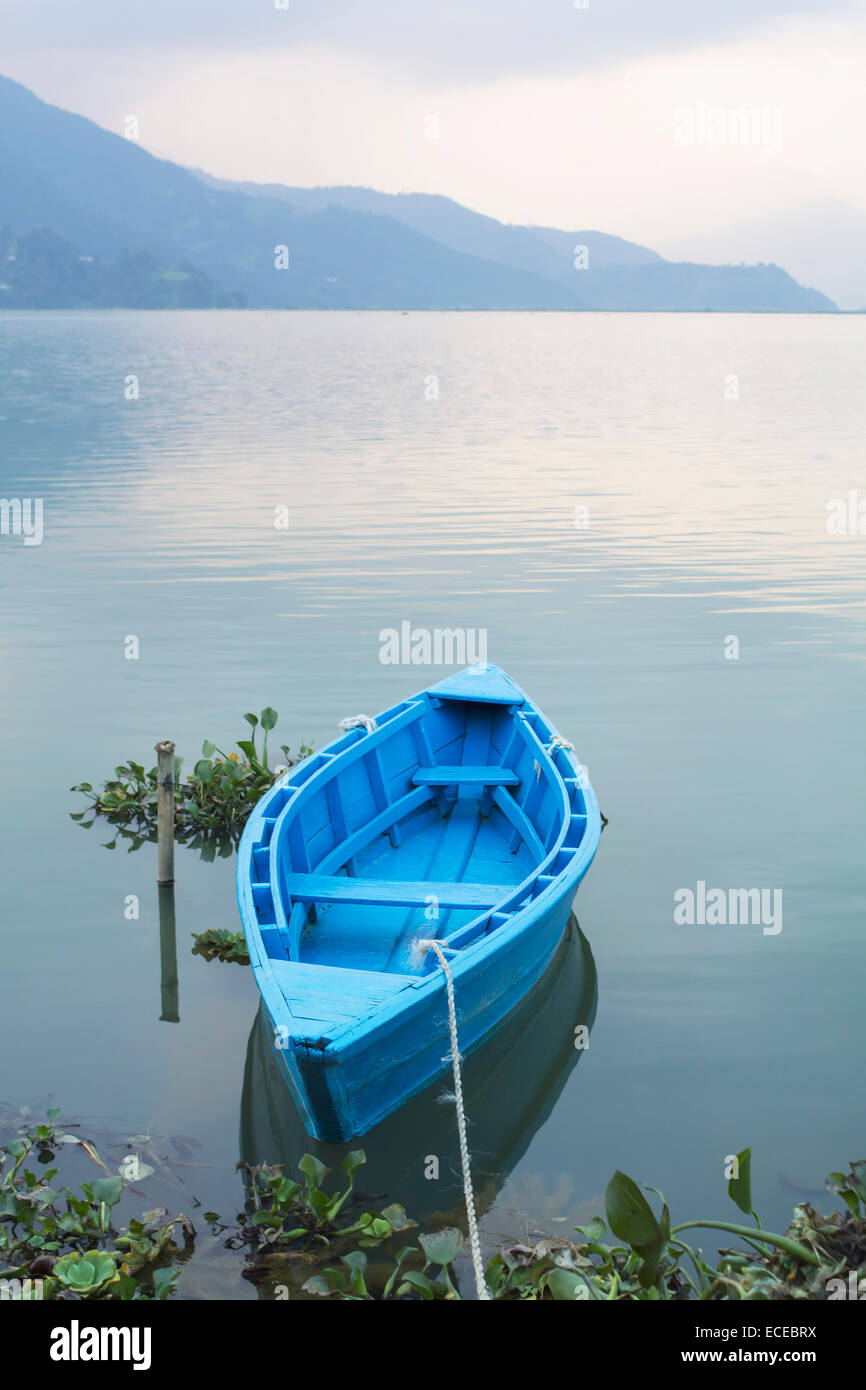 Nepal, Western Region, Gandaki Zone, Pokhara, Mansawar, Phewa See, blaue Ruderboot in See mit Silhouette des Berges im Hintergrund verankert Stockfoto