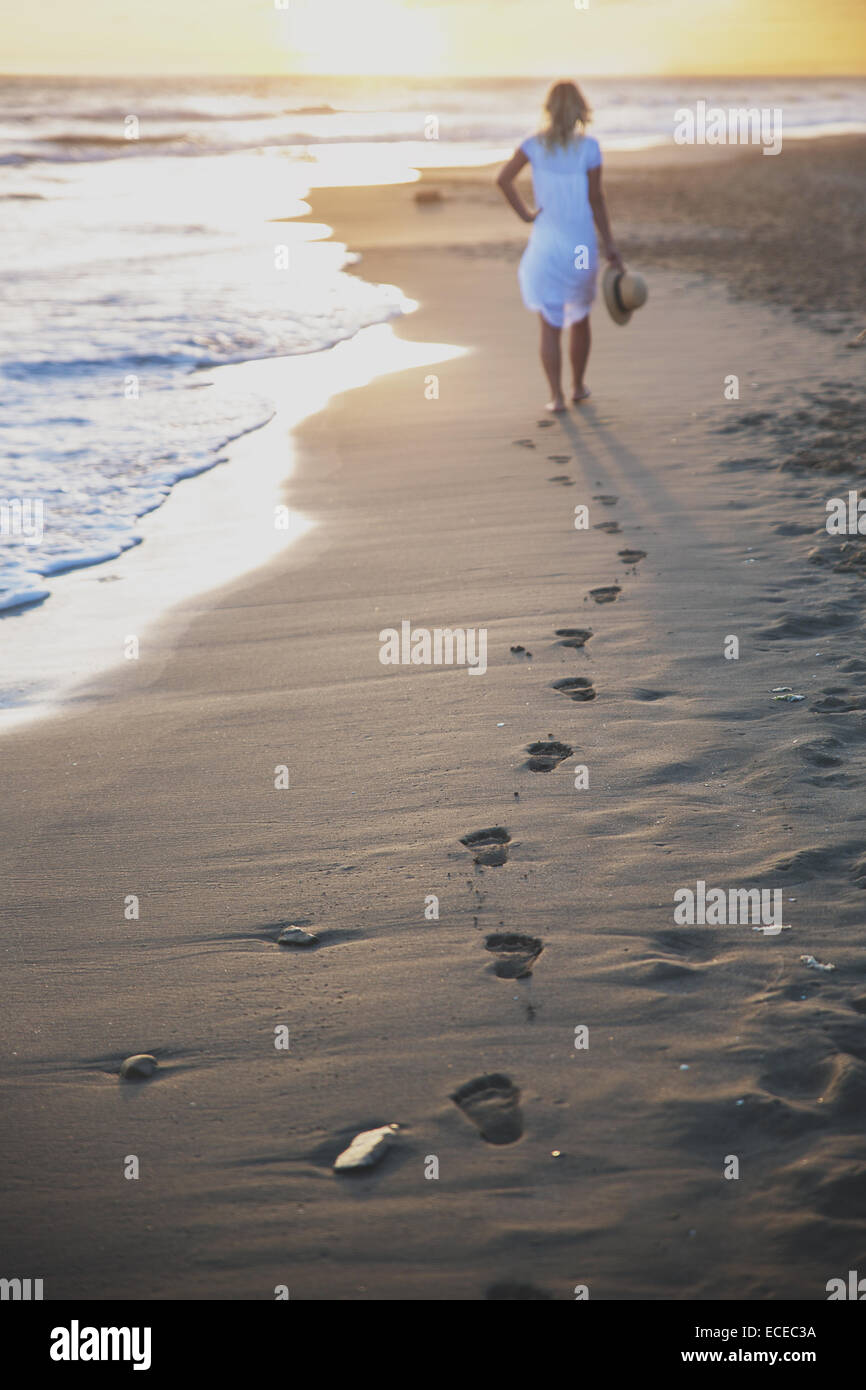 Schöne Frau am Strand mit ihren Fußspuren zurück Stockfoto