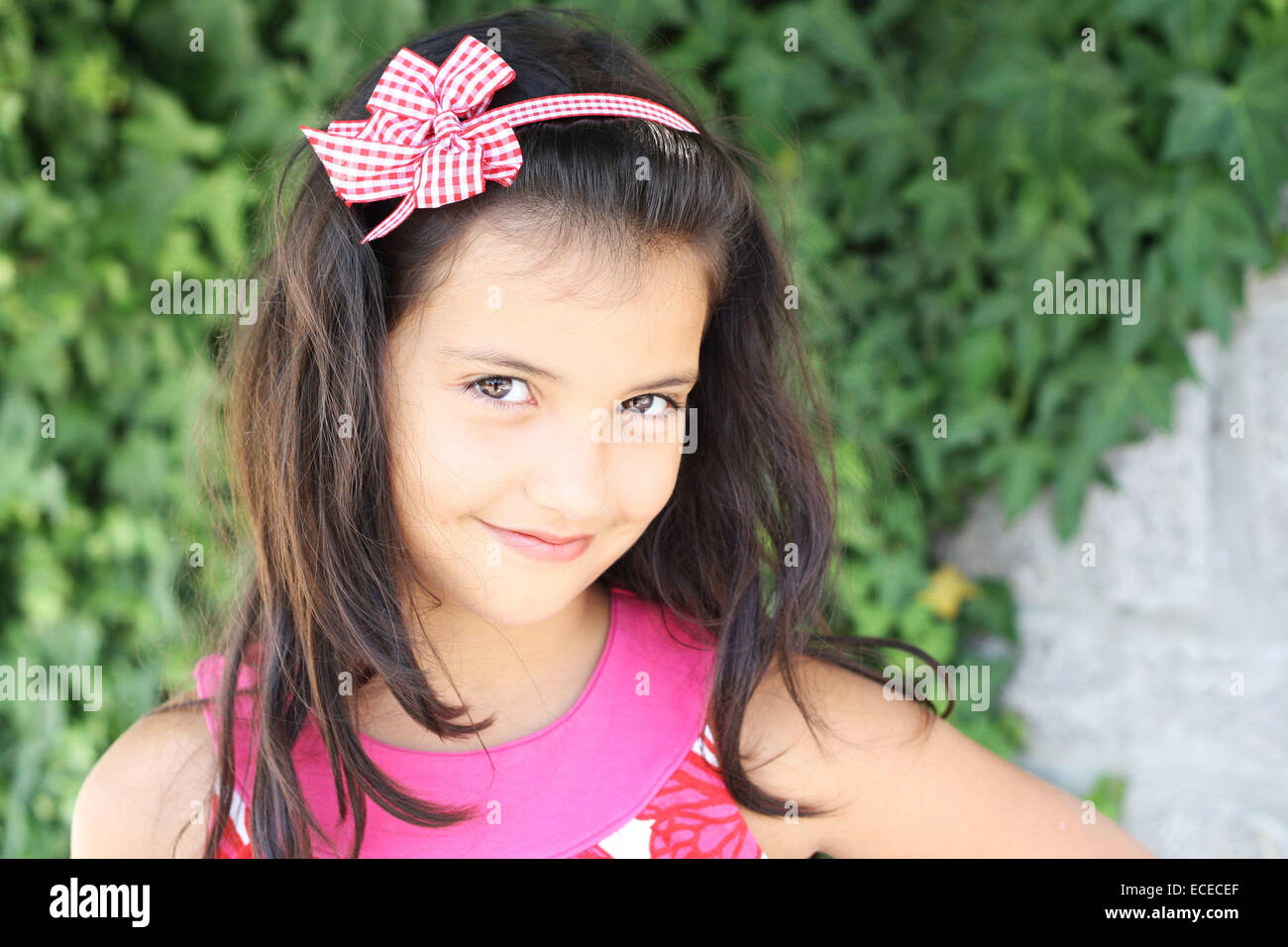Süßes Lächeln auf den Lippen kleines Mädchen (6-7) mit langen dunklen Haaren auf grünen Efeu Hintergrund Stockfoto