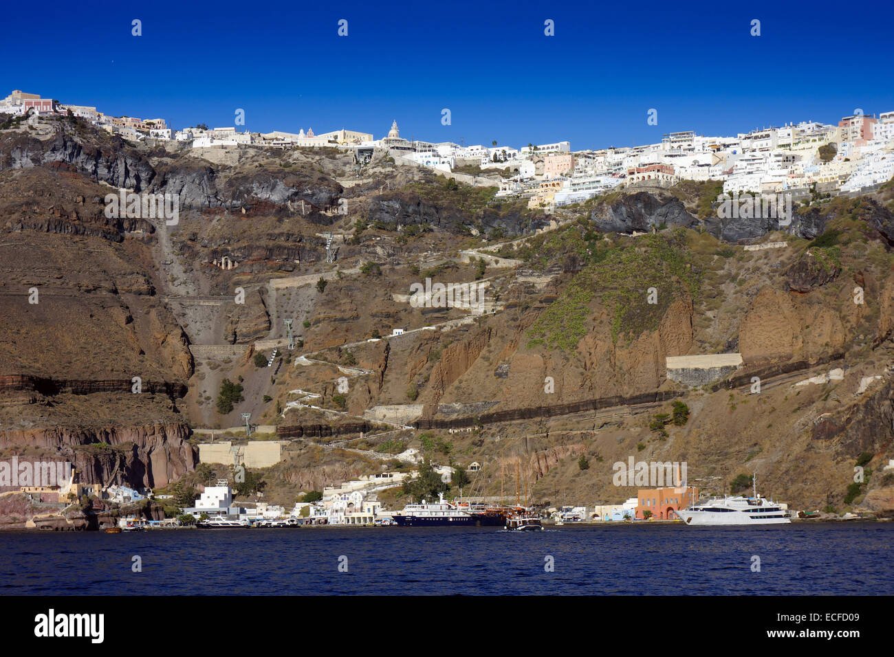 Weiße Häuser vom blauen Meer am Rand der Caldera, Vulkankrater, Santorin mit festgemachten Jachten und Zick-Zack-Esel Weg Stockfoto