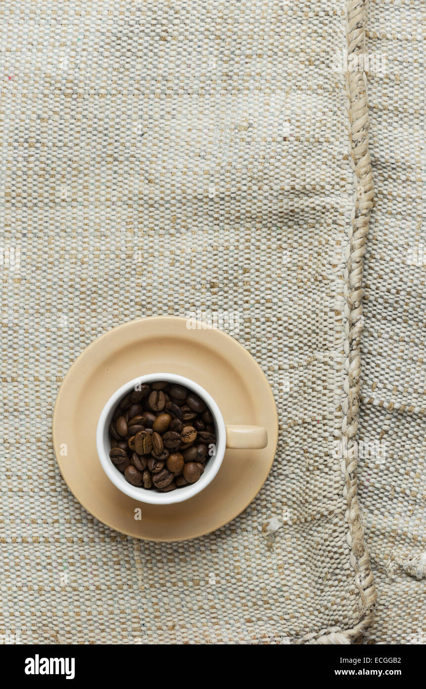 Kaffeebohnen in eine Tasse über rustikale Sackleinwand, über Ansicht Stockfoto
