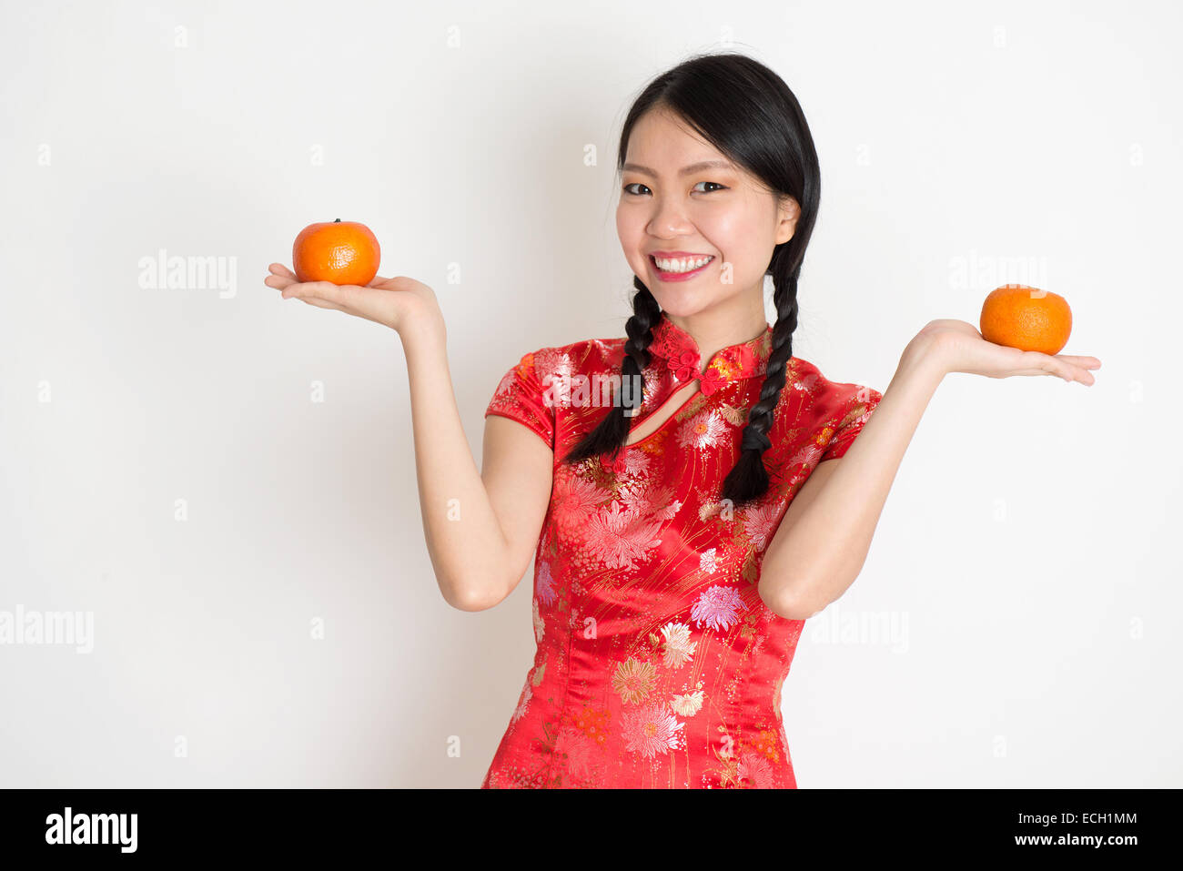 Porträt des chinesischen Asiatin Hände halten Mandarine orange, im traditionellen roten Qipao stehen auf einfarbigen Hintergrund. Stockfoto